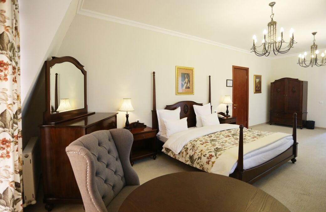 A bedroom with a four-poster bed, a chair, a dresser, a mirror, and a chandelier.