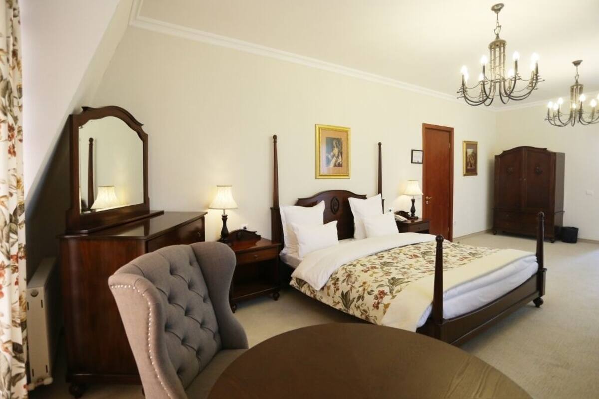 Un dormitorio con cama con dosel, una mesita de noche de madera, una silla, un aparador y una araña.