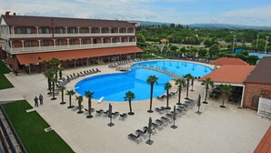 A hotel with a large swimming pool, outdoor seating, and a view of the surrounding landscape.