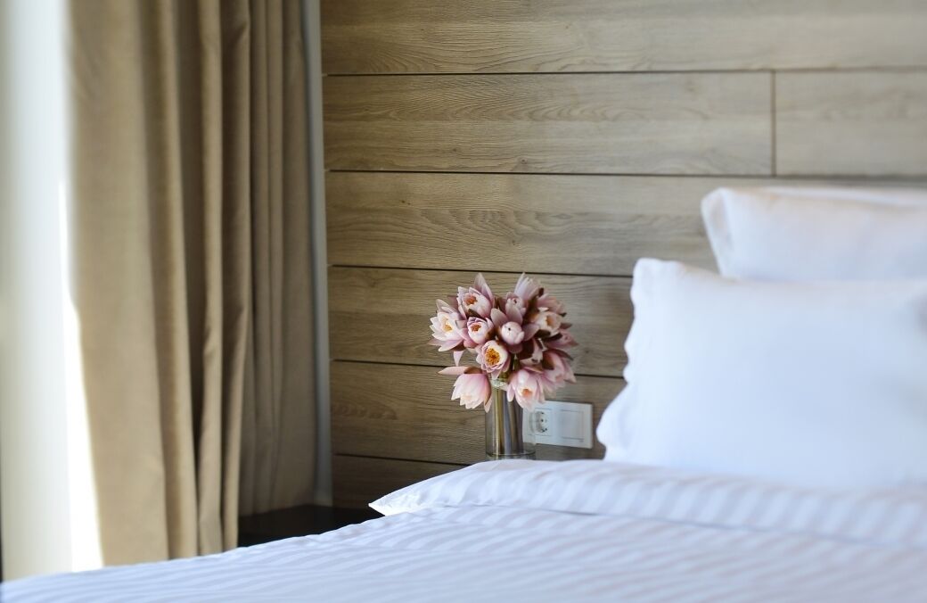 A hotel room with a wooden wall, a bed with white bedding, and a vase of flowers on a nightstand.