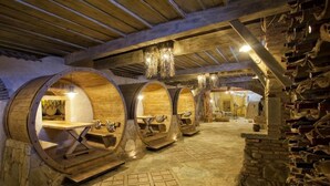 A rustic cellar with wooden barrel seating, stone walls, and a chandelier.