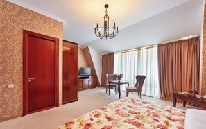 Habitación de hotel con una cama grande, un escritorio con silla, televisión y candelabro.