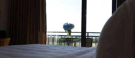 A hotel room with a large bed, a window with curtains, and a view of greenery outside.