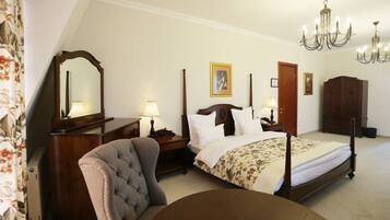 A bedroom with a four-poster bed, a wooden dresser, a chair, and a chandelier.