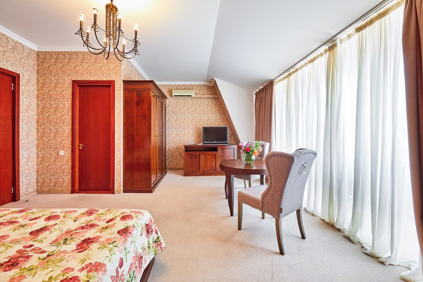 A hotel room with a bed, a desk with a TV, a chair, and a window with curtains.
