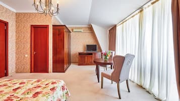 Habitación de hotel con cama, escritorio con televisor, silla y ventana con cortinas.