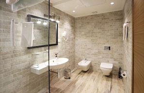 Un baño moderno con lavamanos, bidé e inodoro, con diseño de pared de ladrillo y cabina de ducha de vidrio.