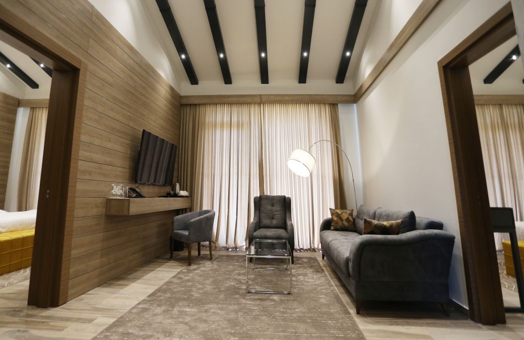 A modern living room with a sofa, armchair, and a desk with a flat-screen TV.