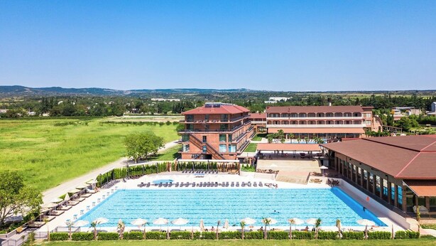 A hotel with a large swimming pool, multiple buildings, and a surrounding grassy area.