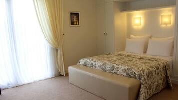 A bedroom with a bed, a bench, a picture on the wall, and two wall-mounted lights.