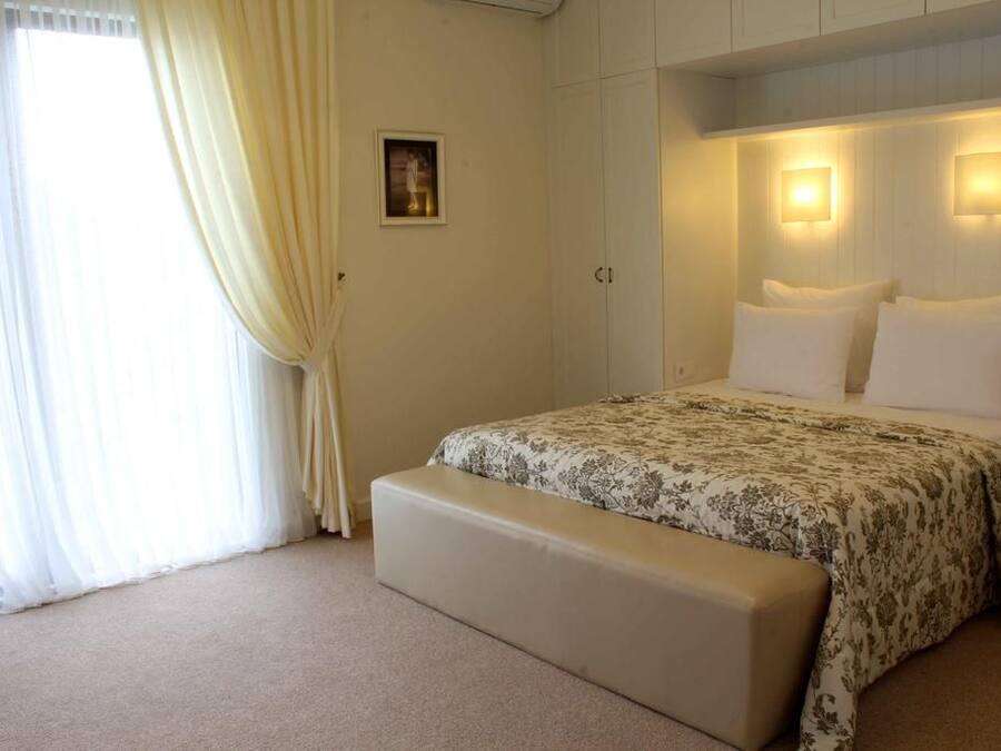 A bedroom with a bed, a bench, a picture on the wall, and two wall-mounted lights.