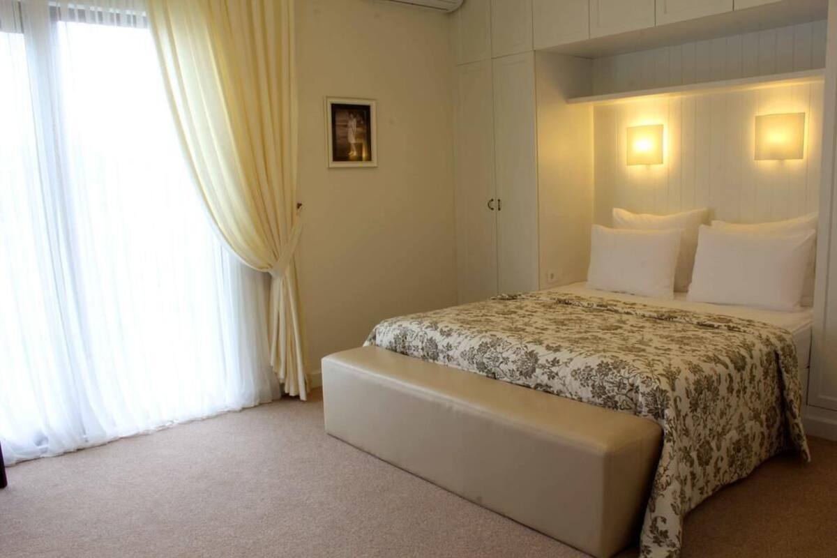 Un dormitorio con una cama, un banco, un cuadro en la pared y dos lámparas fijadas a la pared.