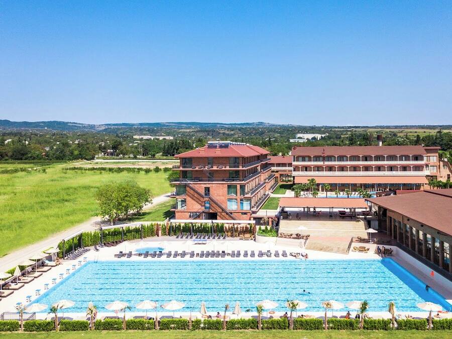 A hotel with a large swimming pool, multiple buildings, and a surrounding grassy area.