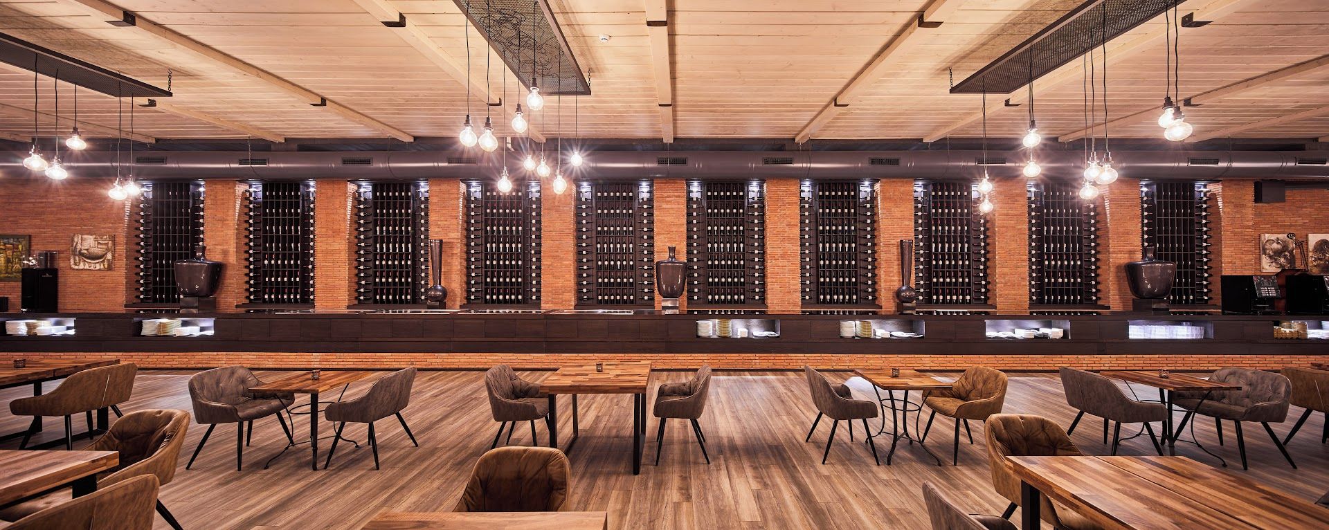 Un'area bar con tavoli e sedie in legno, una scaffalatura per bottiglie di vino e lampadari.
