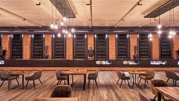 Un'area bar con tavoli e sedie in legno, una scaffalatura per bottiglie di vino e lampadari.