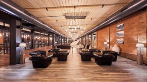 Ein geräumiger Lounge-Bereich mit Ledersofas, einem Flügel und einem langen Korridor mit Holzdielen und Backsteinwänden.