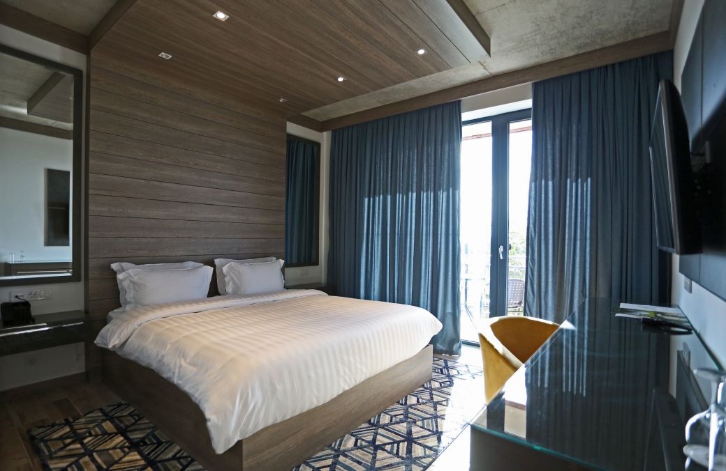 A modern hotel room with a large bed, a glass table, and a view of the outdoors.