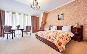 Habitación de hotel con una cama grande, dos sillones, una mesita y un candelabro.