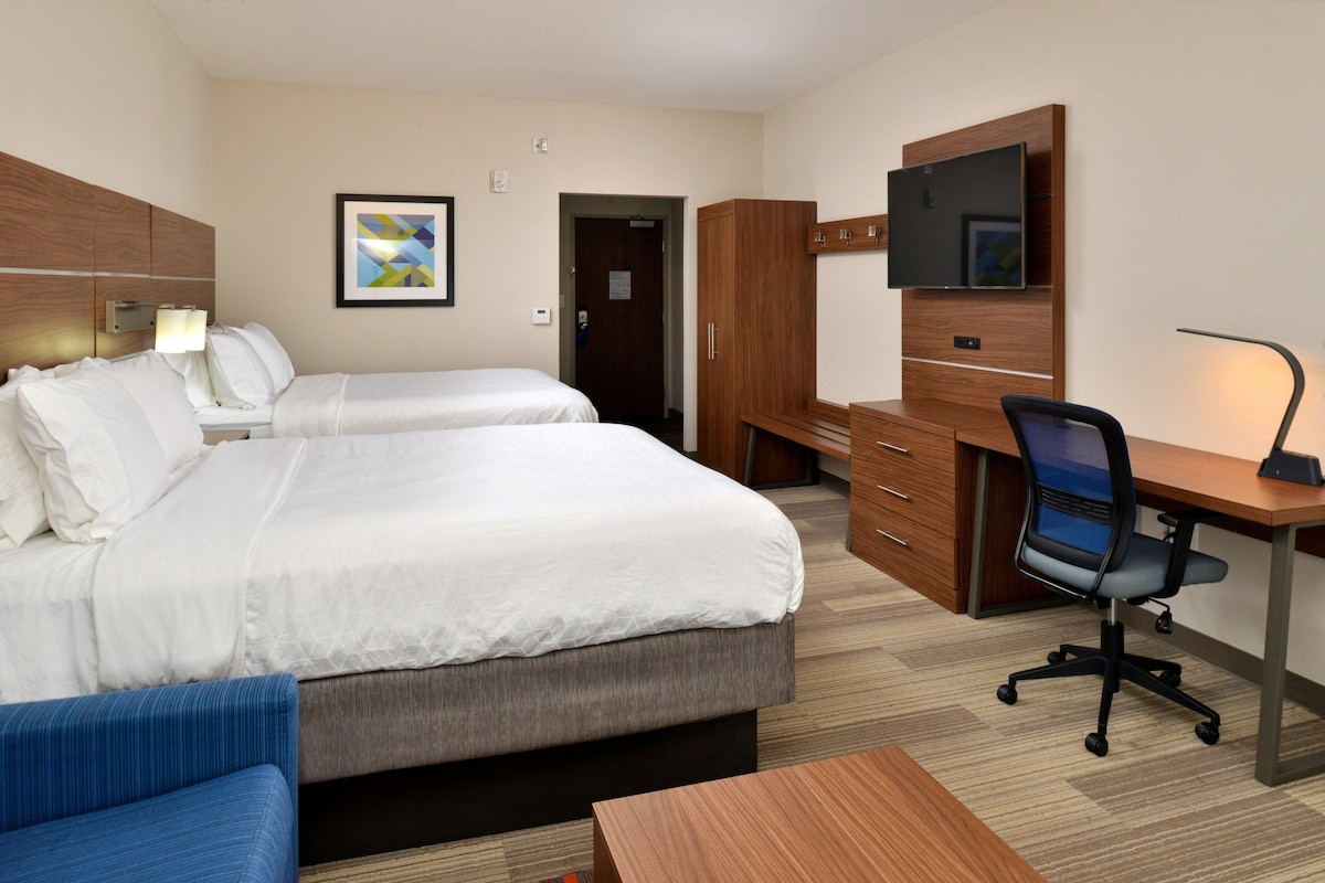 Une chambre d’hôtel avec deux lits, un bureau, une chaise, une télévision et une armoire.