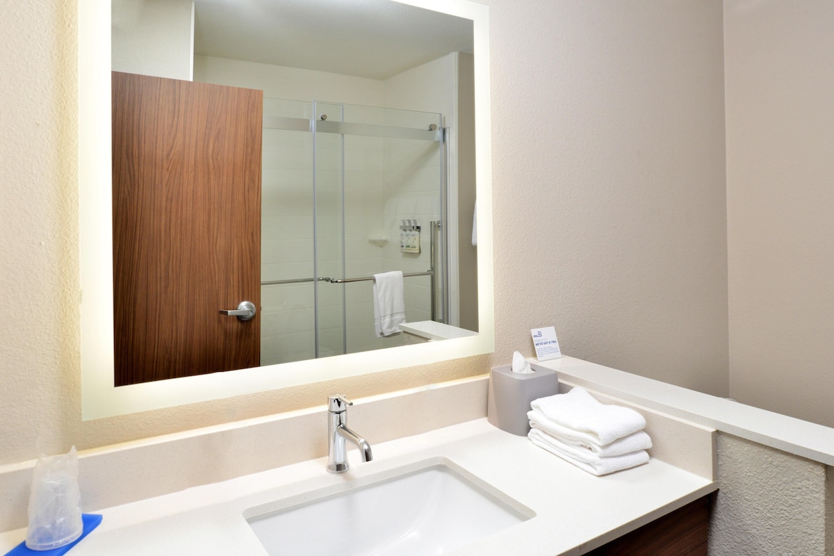 Une salle de bain avec un grand miroir, un lavabo blanc, une douche en verre et un porte-serviettes avec des serviettes pliées.
