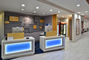 Zona de recepción de hotel con dos mostradores, un reloj en la pared y una máquina expendedora.