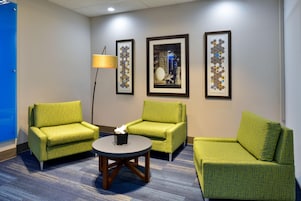 Una habitación de hotel con dos sillones verdes, una mesita redonda y tres cuadros en la pared.