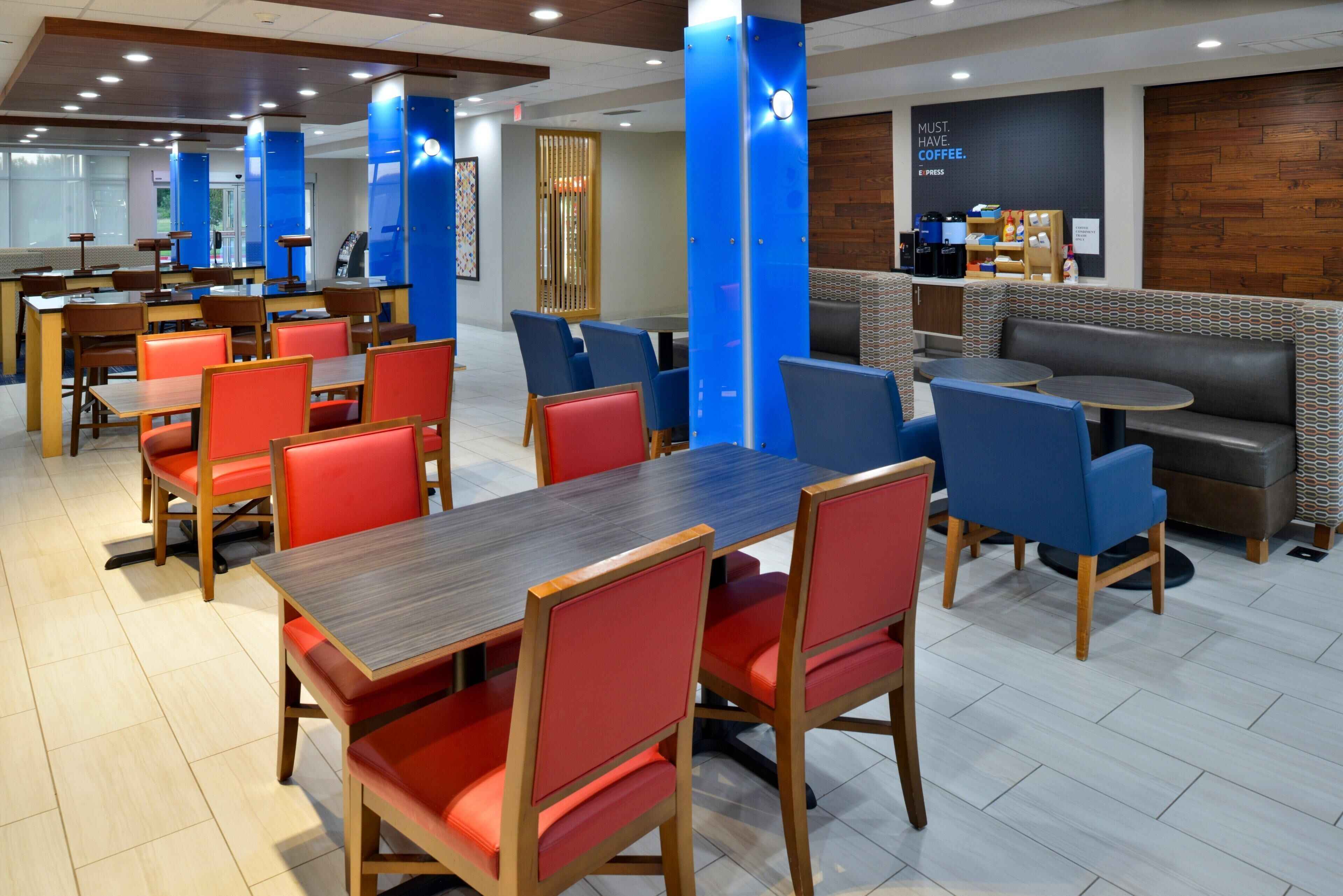 Un ristorante moderno con tavoli e sedie in legno, un'area bar e un angolo salotto con cuscini decorati.