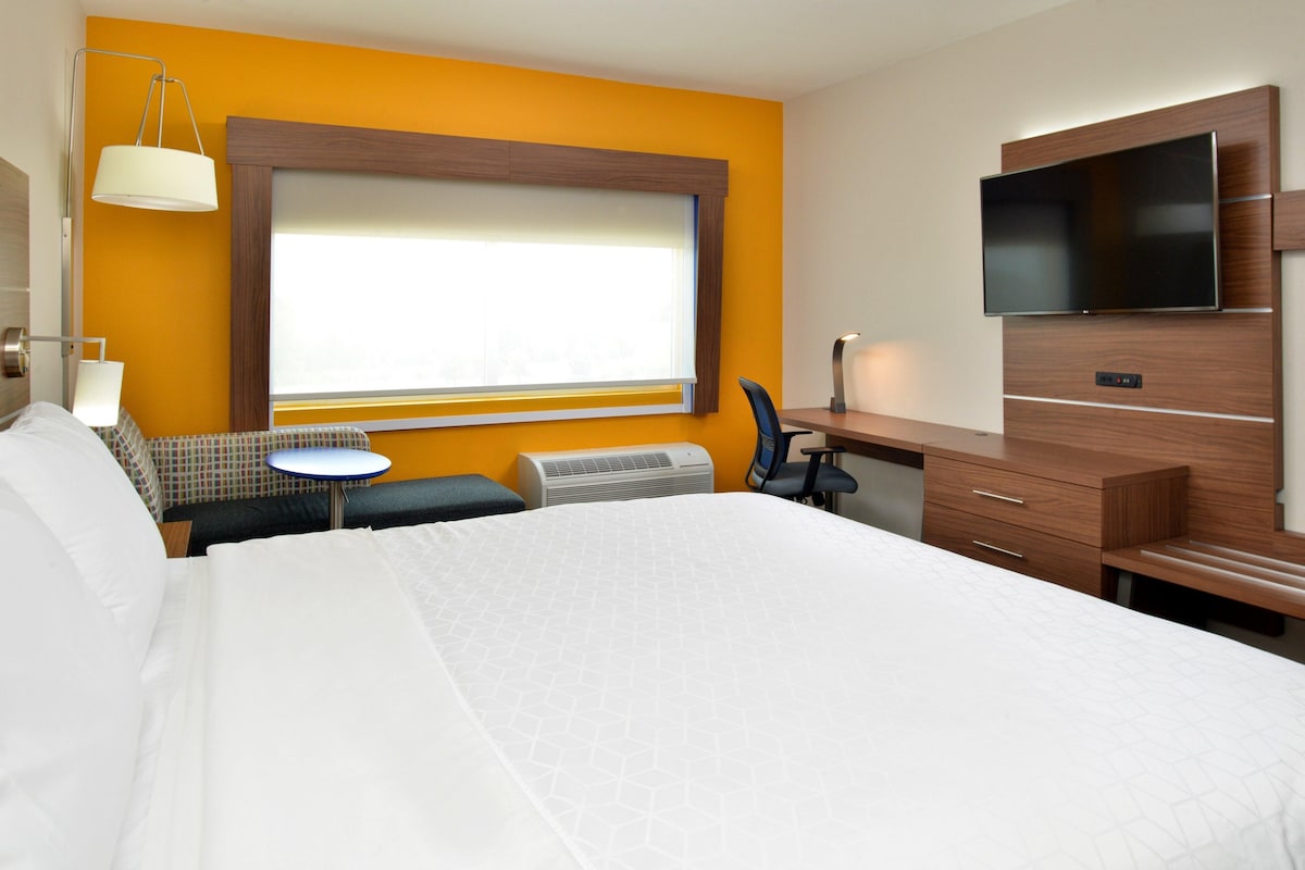 Une chambre d’hôtel avec un grand lit, un bureau avec une chaise, un téléviseur à écran plat et une fenêtre avec des stores.
