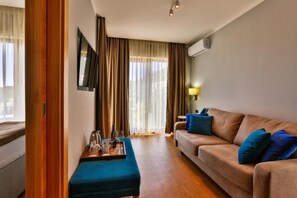 A room with a sofa, a coffee table with glasses, a TV mounted on the wall, and a window with curtains.