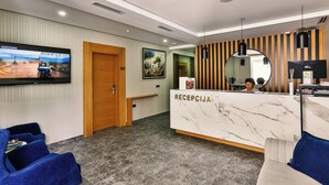A hotel reception area with a marble reception desk, a television mounted on the wall, and a seating area with blue chairs. - Lusso Mare (Boreti)