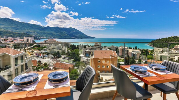 A table set for two with a view of a coastal city and mountains. - Lusso Mare (Boreti)