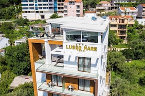 A modern hotel with a glass balcony, outdoor seating, and a view of the surrounding neighborhood. - Lusso Mare (Boreti)