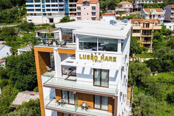 A modern hotel with a glass balcony, outdoor seating, and a view of the surrounding neighborhood. - Lusso Mare (Boreti)