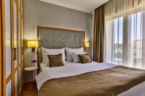 A hotel room with a large bed, two bedside lamps, a wooden nightstand, and a view of the outdoors through sheer curtains. - Lusso Mare (Boreti)