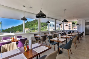 A restaurant with tables and chairs, large windows, and hanging pendant lights. - Lusso Mare (Boreti)