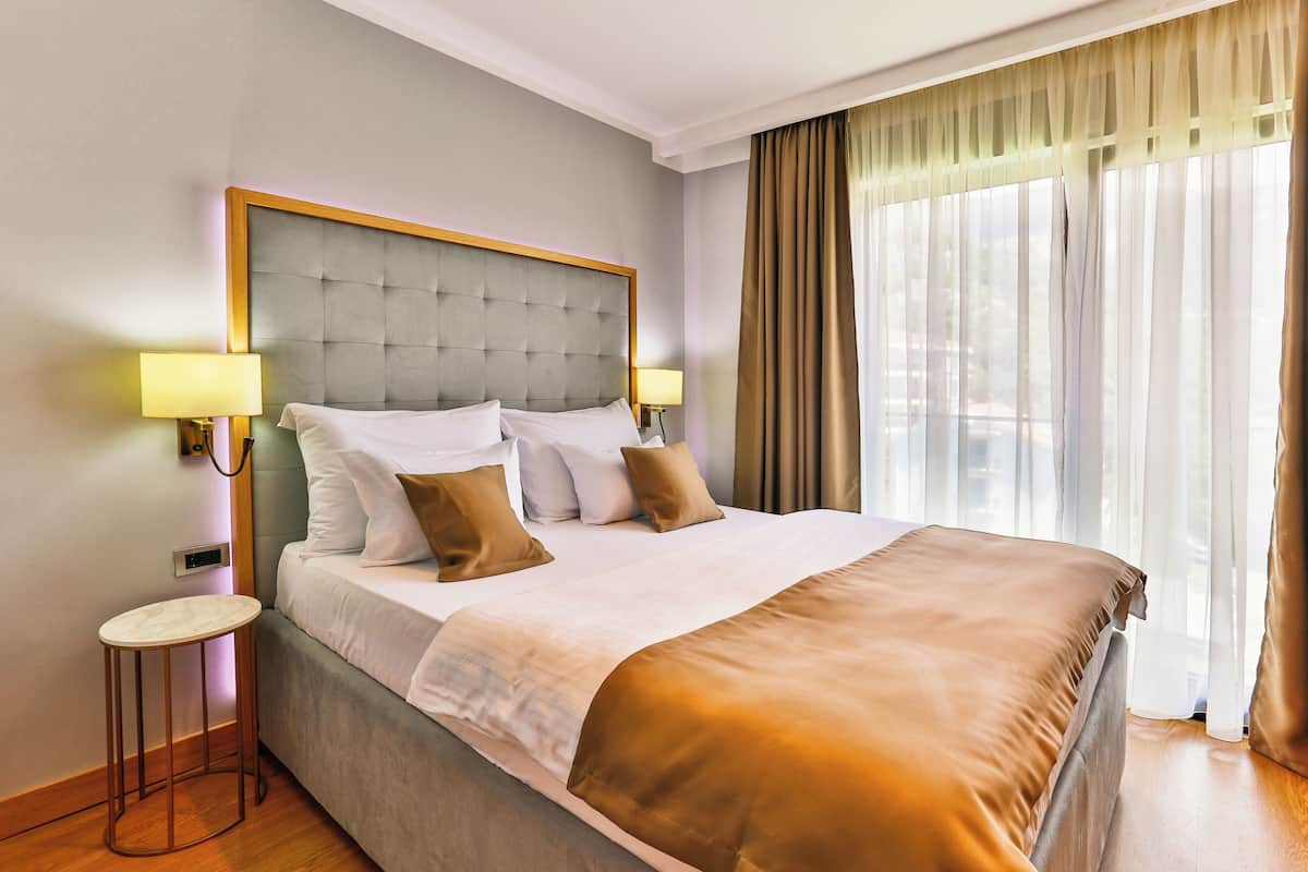 Une chambre d’hôtel avec un grand lit, deux lampes de chevet, une petite table et une fenêtre avec des rideaux.