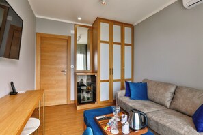 Un espacio habitable compacto con un escritorio de madera, un sofá, una mesa de centro y un mueble con puertas de vidrio.