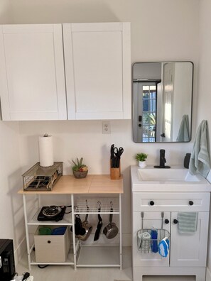 Eine Küche mit weißen Schränken, einer Holzausziehtafel, einem Spülbecken, einem Spiegel und einem kleinen Topfpflanzen.