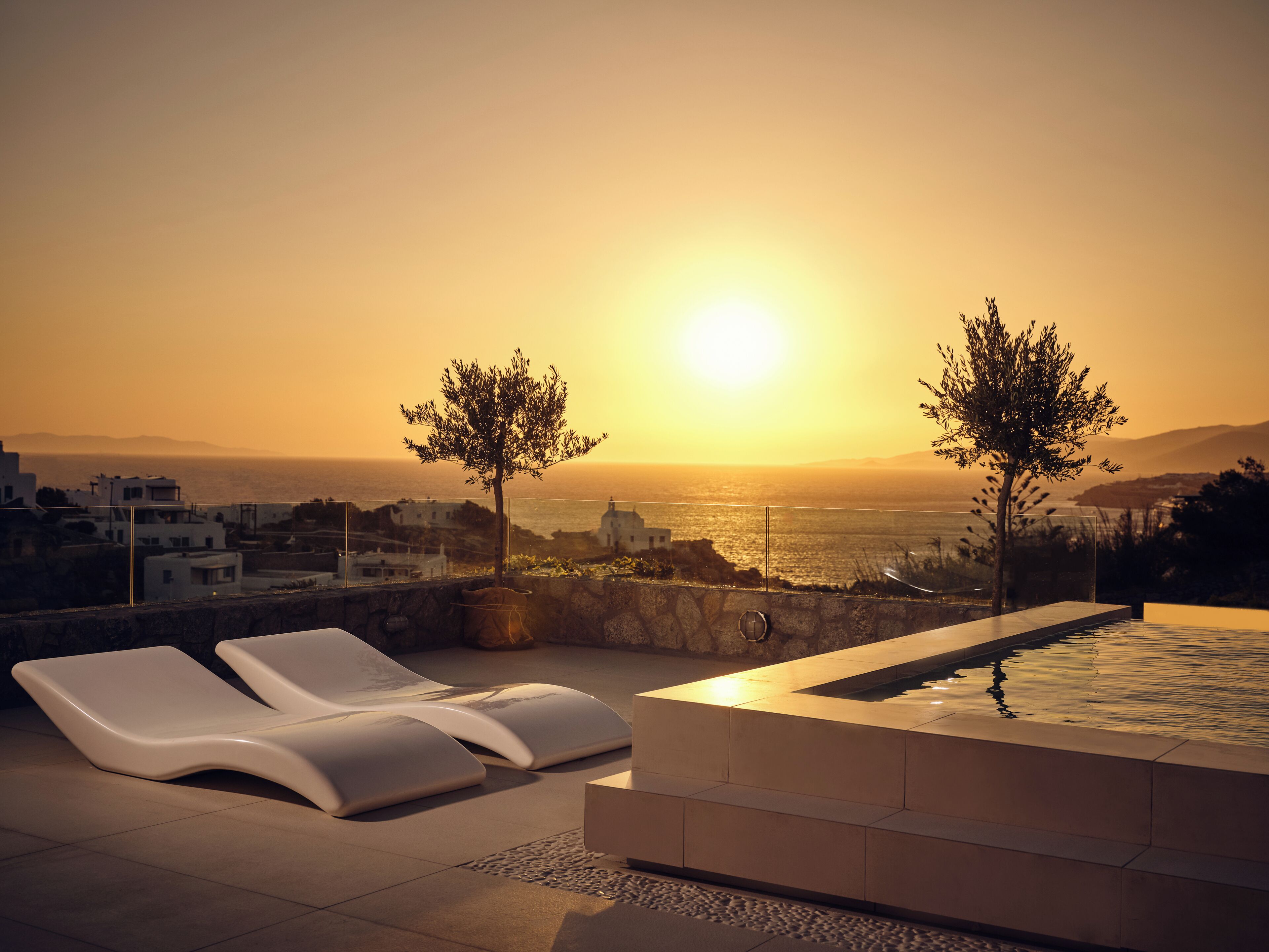 A rooftop terrace with lounge chairs, a pool, and a sunset view.