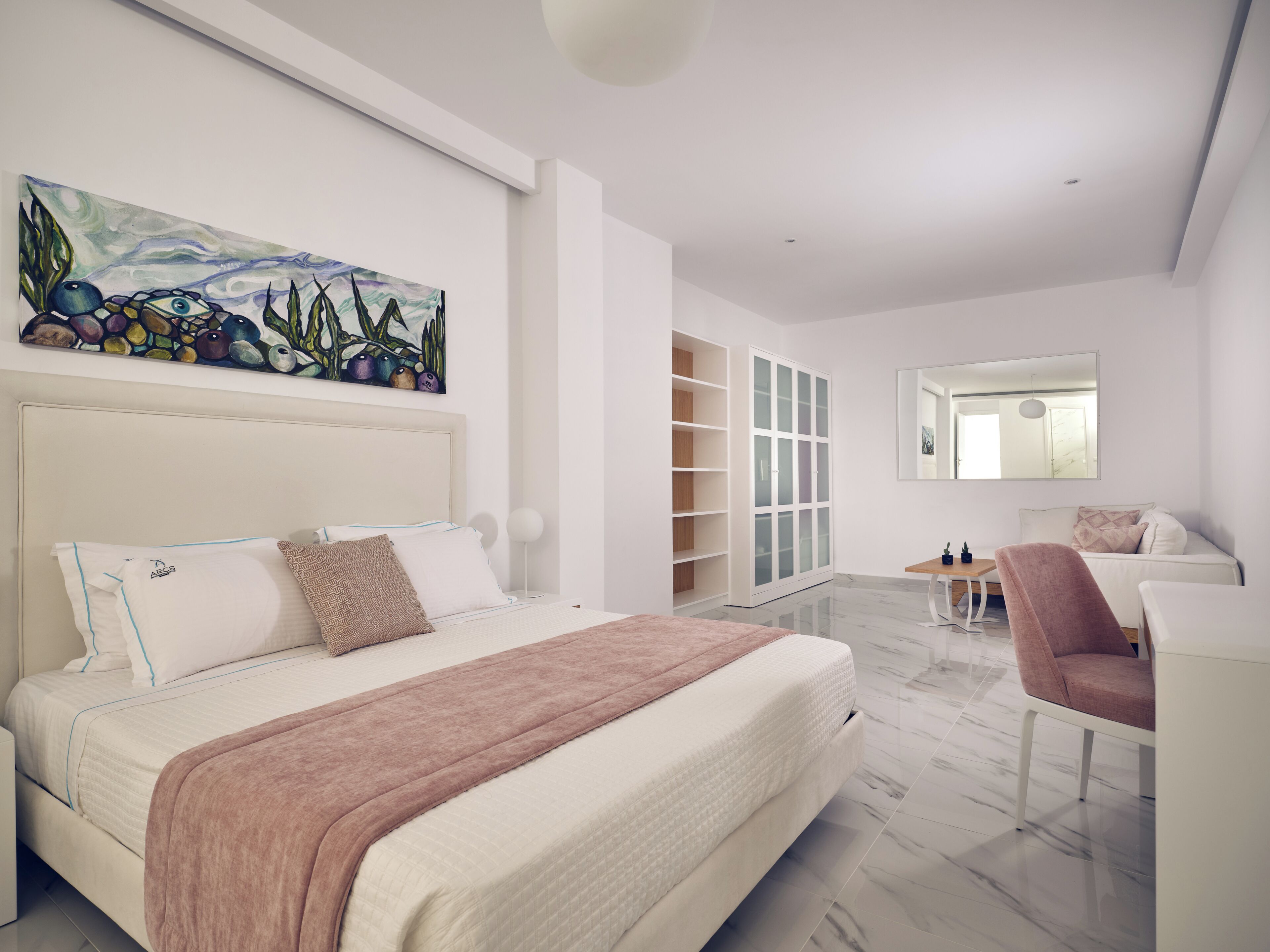A modern bedroom with a large bed, a painting, a wardrobe, a mirror, and a seating area.