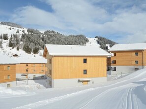 Complejo de edificios cubiertos de nieve con varias estructuras de madera, rodeado de un paisaje nevado y un cielo despejado.