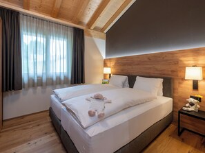 A hotel room with a large bed, wooden ceiling beams, a nightstand with a lamp, and a window with curtains. - Pradas Resort Brigels, (Breil/Brigels), 65055B by Interhome (Breil/Brigels)