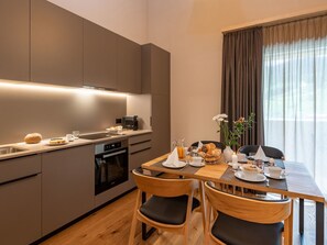 A modern kitchen with a dining area, featuring a built-in oven, a coffee machine, and a breakfast setup with bread, eggs, and a pitcher of orange juice. - Pradas Resort Brigels, (Breil/Brigels), 65055B by Interhome (Breil/Brigels)
