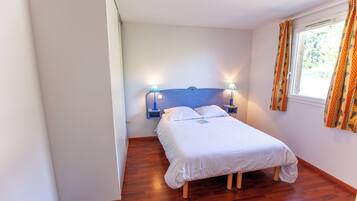 A small, neatly arranged bedroom with a single bed, two bedside lamps, and a window with curtains.