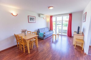 A room with a dining table, chairs, a sofa, a small desk, and a television. - Olydea la Chalosse (Cassen)