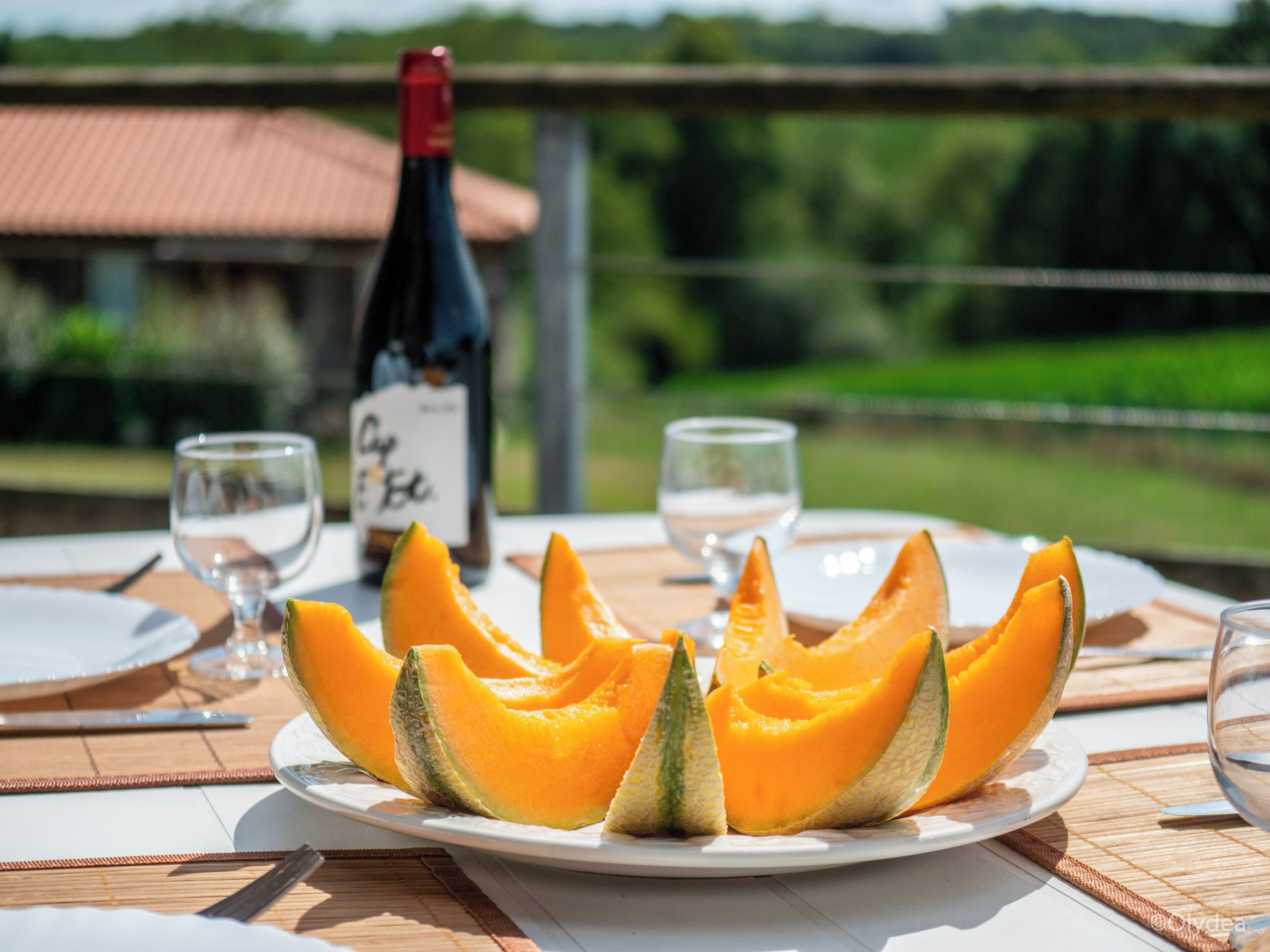 A dining table with a plate of cantaloupe, two wine glasses, and a wine bottle.
