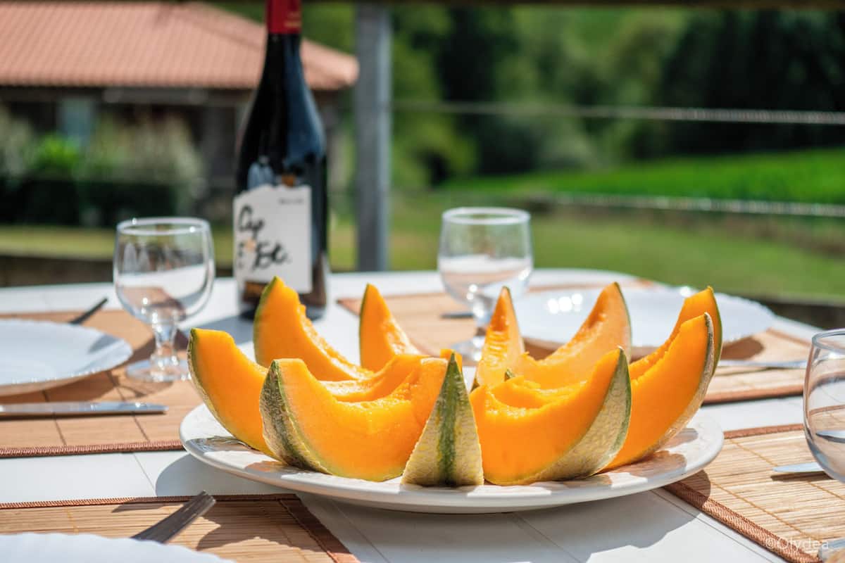 A dining table with a plate of cantaloupe, two wine glasses, and a wine bottle.