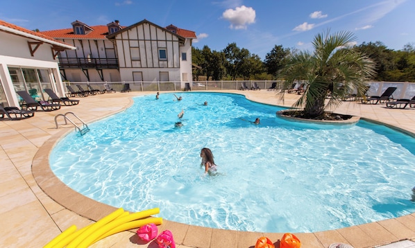 A swimming pool with multiple people, lounge chairs, and a palm tree. - Olydea la Chalosse (Cassen)