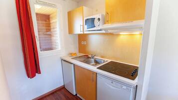 Una cocina compacta equipada con microondas, estufa, lavaplatos y fregadero.
