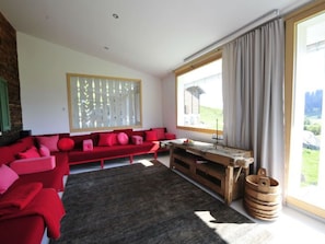Ein modernes Wohnzimmer mit einem roten Sofa, einem Holztisch und einem großen Fenster mit Vorhängen.